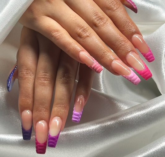 Two female hands on top of each other with long length nails and several shades of pink and purple polish on the tips of the fingernails