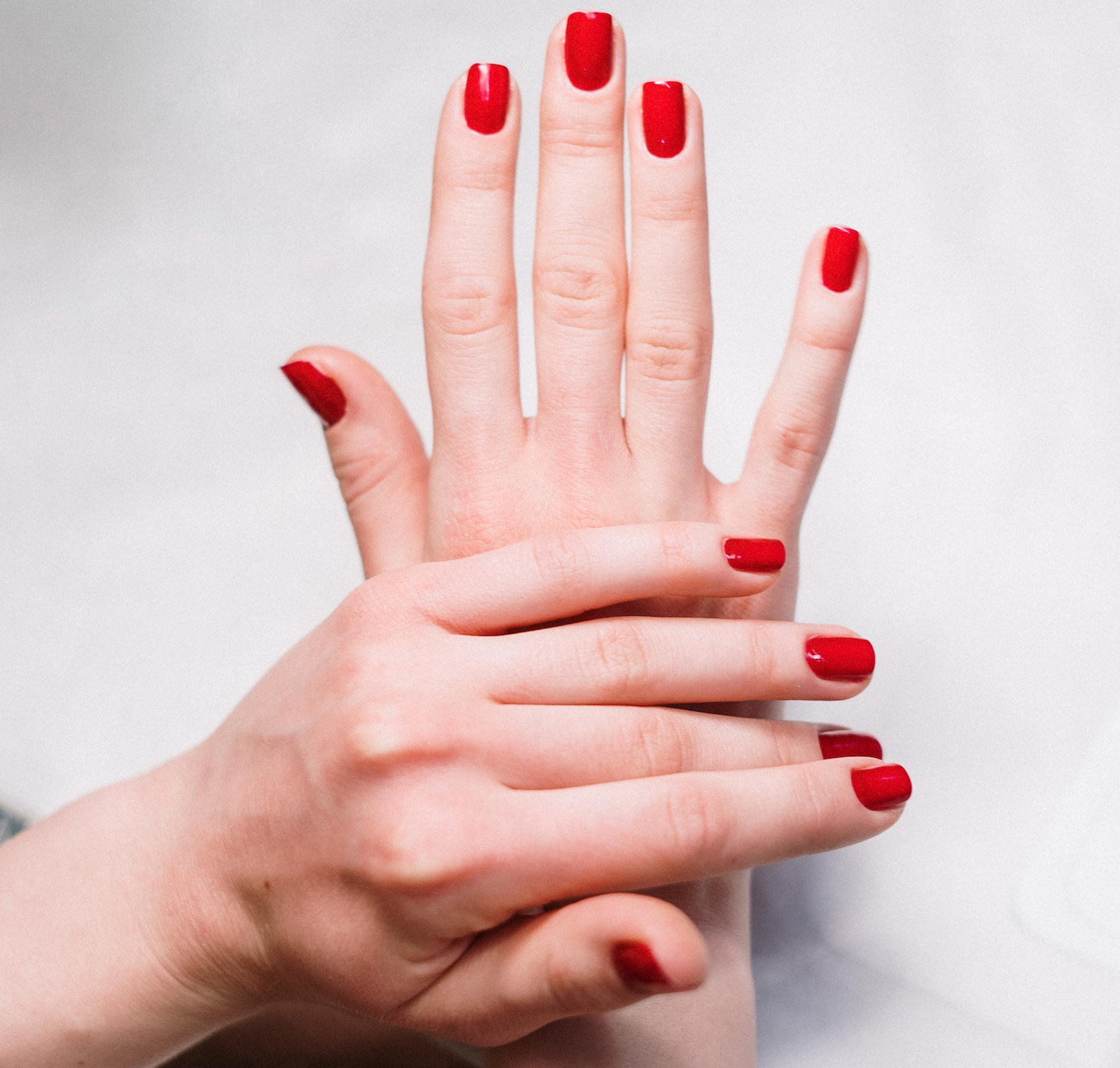 Close-up of hands of a white female on top of each other with pure red colored polish on the fingernails