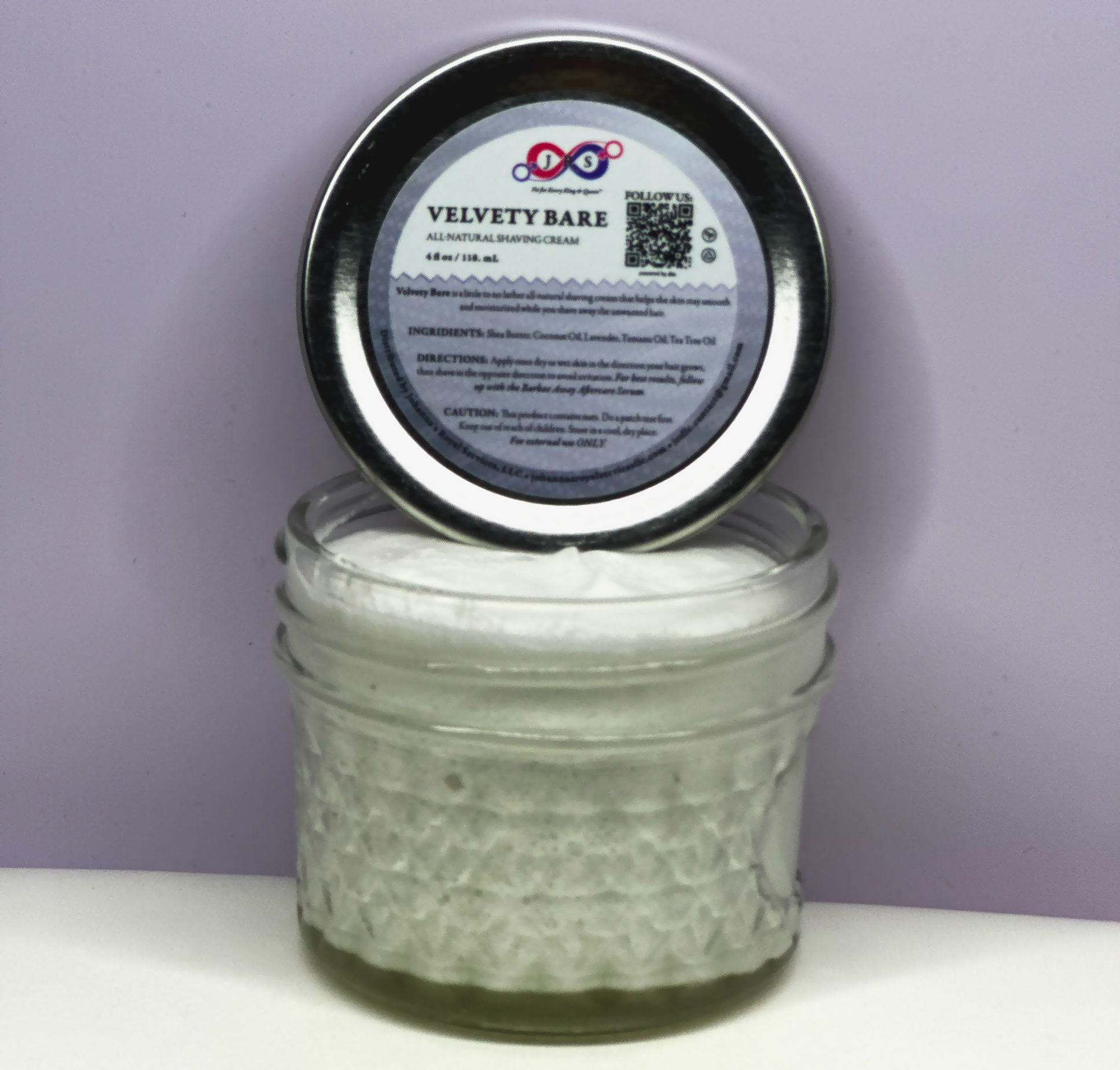 An opened jar of Velvety Bare Shaving Cream with the lid resting on the top and showing the product content