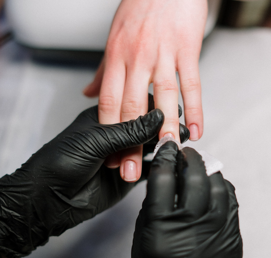 Close-up of hands of a manicurist wearing black latex glolves while polishing the ring finger nail of a white female's hand