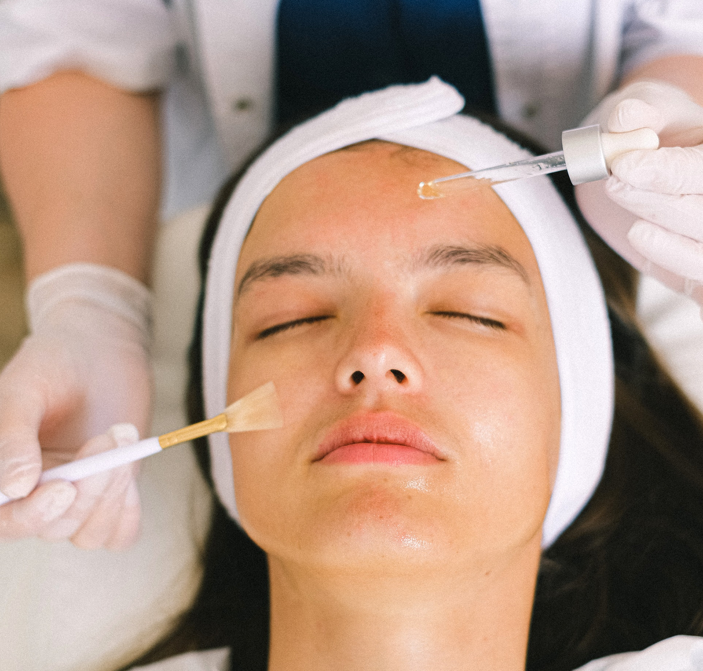 Close-up of a white woman's face with the hands of a beautician applying a chemical peeling with a dropper and brush