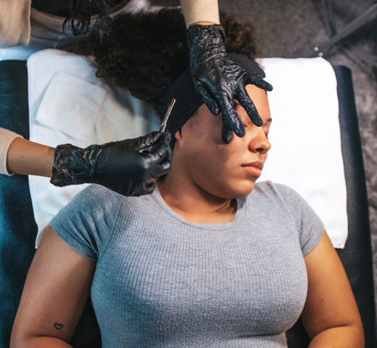 Close-up of a black woman laying on her back while receiving a dermaplane from an esthetician wearing black gloves