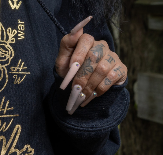Close-up of a woman's hand with extra long length nails, peach color polish and one stone decoration on each nail
