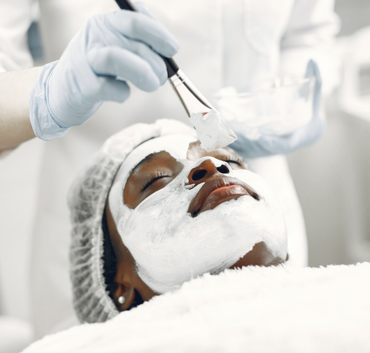 Close-up of a black woman's face receiving a facial from and esthetician using a brush