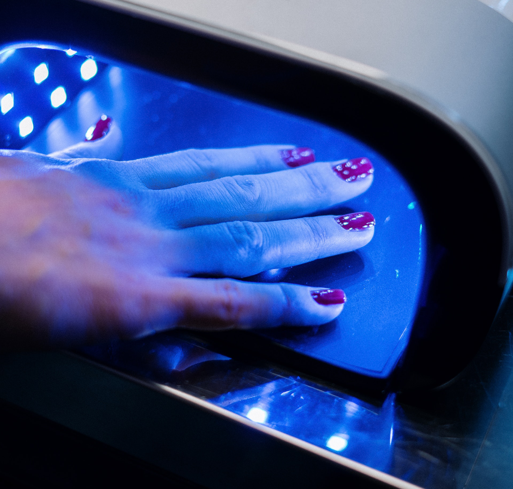 Hand of a white woman with read color polish on her fingernails and getting them dried with UV light