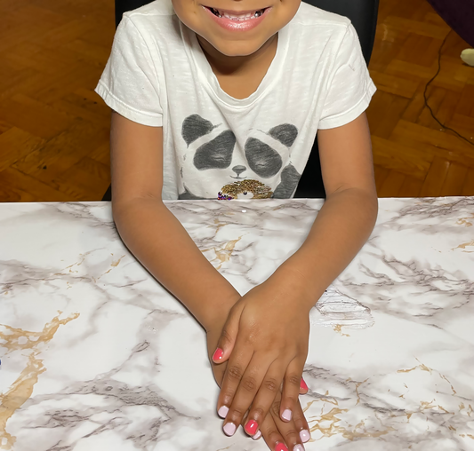 Close-up of a happy 4 years old girl with her hands on top of each other on a table after getting pink nail polish on her fingernails